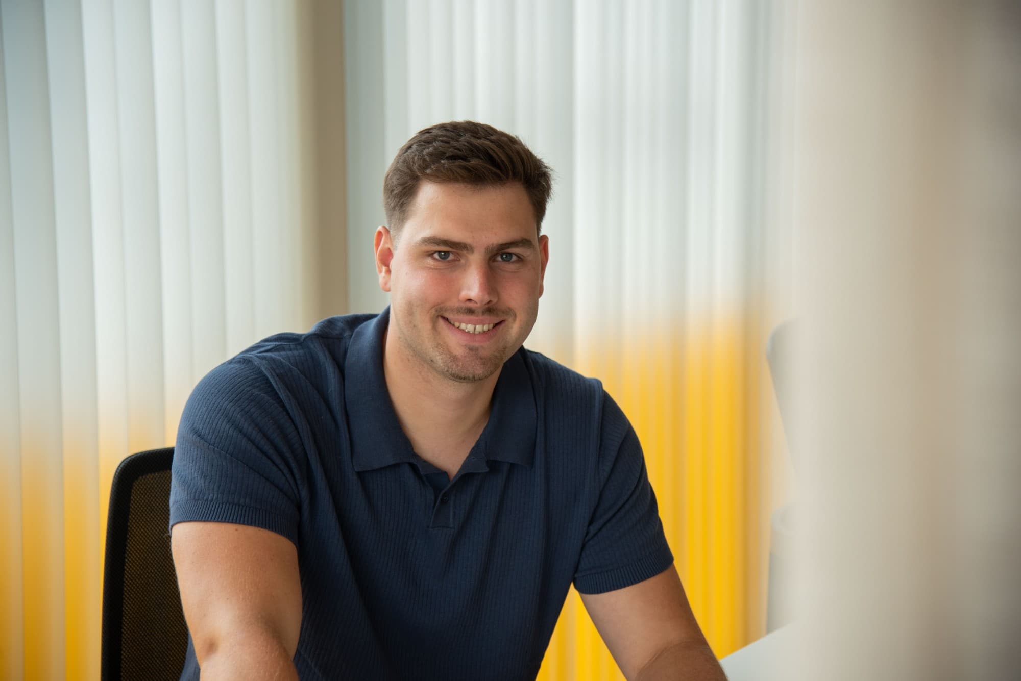 Portrait of Mozes Vanlimburg, smiling, in a navy polo at his desk.